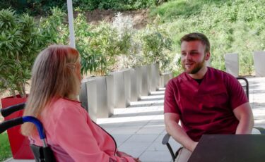 Pflegehilfskraft redet mit Bewohnerin im Rollstuhl