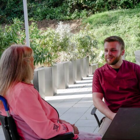 Pflegehilfskraft redet mit Bewohnerin im Rollstuhl